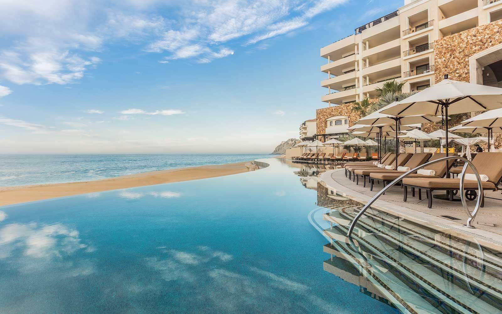 A poolside area with lounge chairs and umbrellas, overlooking a beach and ocean.