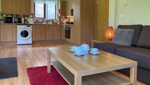 A modern kitchen with wooden cabinets, a washing machine, and a dining area with a table and chairs. - Water Mill Vacations, Badgers Oak (Calbourne)