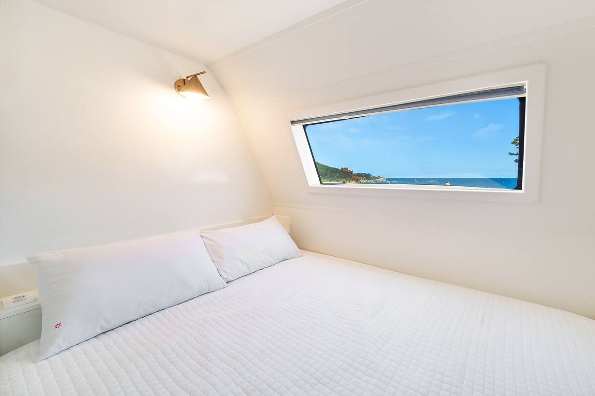 A single-bed room with a window overlooking a beach.