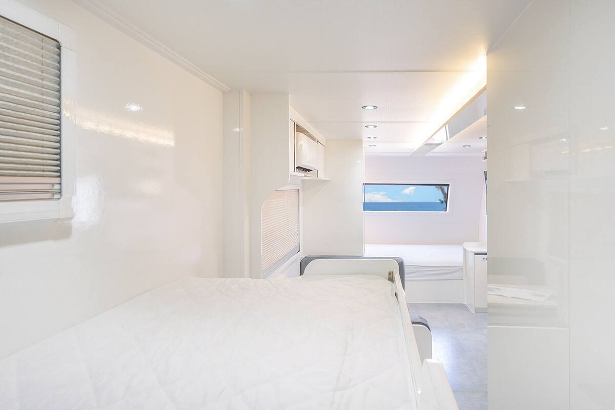 A modern, minimalist bedroom with a bed, a small desk, and a window offering a view of the sea.