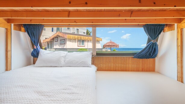 Ein Schlafzimmer mit Bett, Holzboden und Blick auf Strand und Gebäude.