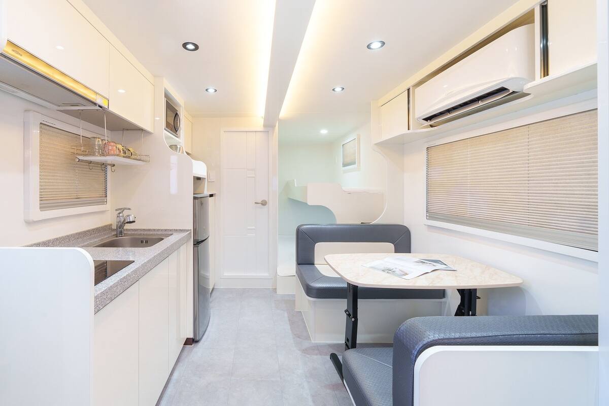 A narrow, well-lit corridor with a kitchenette on one side and a seating area with a table and chairs on the other.