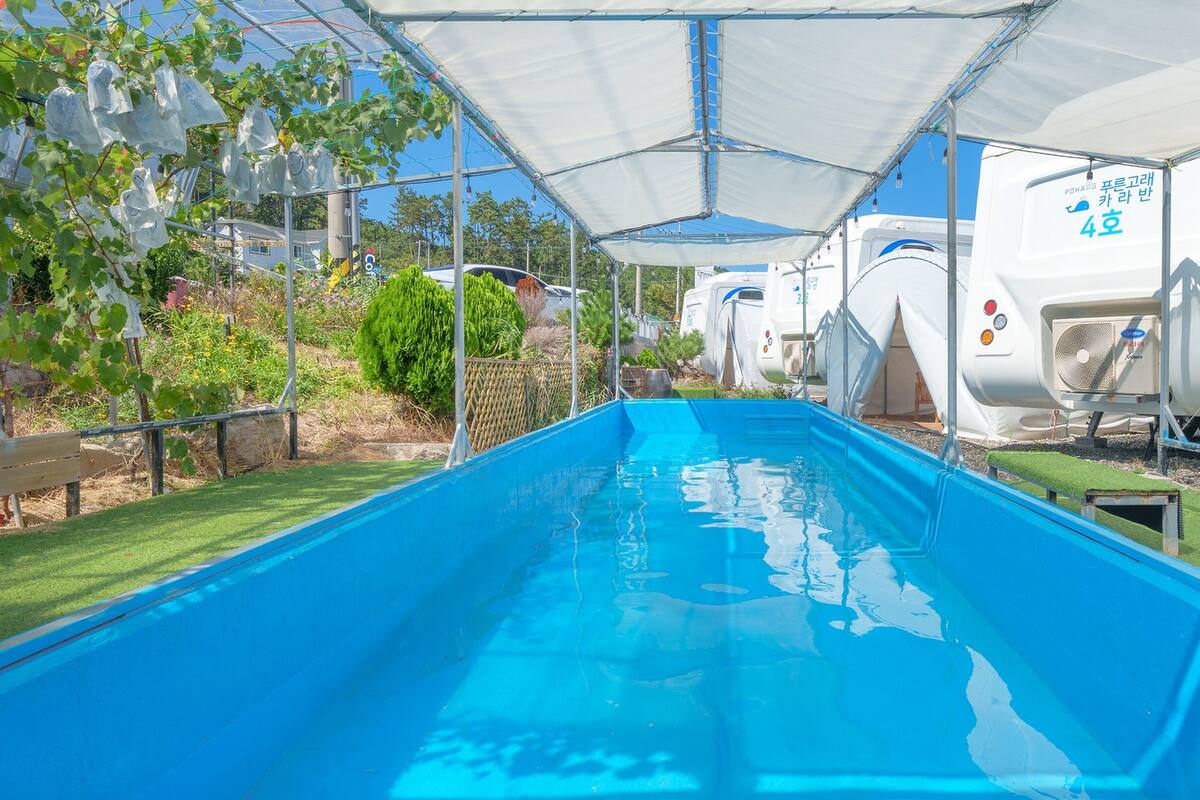A swimming pool under a covered area with RVs parked nearby.