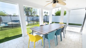 Eine Terrasse mit Holztisch und bunten Stühlen, umgeben von einem weißen Zaun und einem Pool.