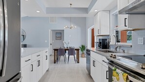 A modern kitchen with white cabinetry, a dining area with a table and chairs, and a central island with a sink and stove. - New Listing! Charlotte Harbor Area Resort, 120mi to Disney & 134mi to Universal - GRH518223 (Englewood)