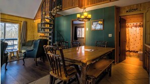 A cozy room with a wooden dining table, chairs, a staircase, and a view of the outdoors.