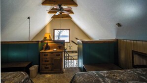 A cozy attic room with a sloped ceiling, a wooden dresser, a lamp, and a view of the outdoors.