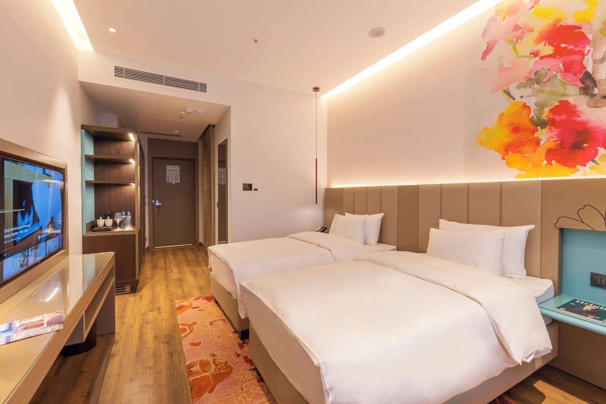 A hotel room with two beds, a TV, a bedside table, and a colorful wall art piece.