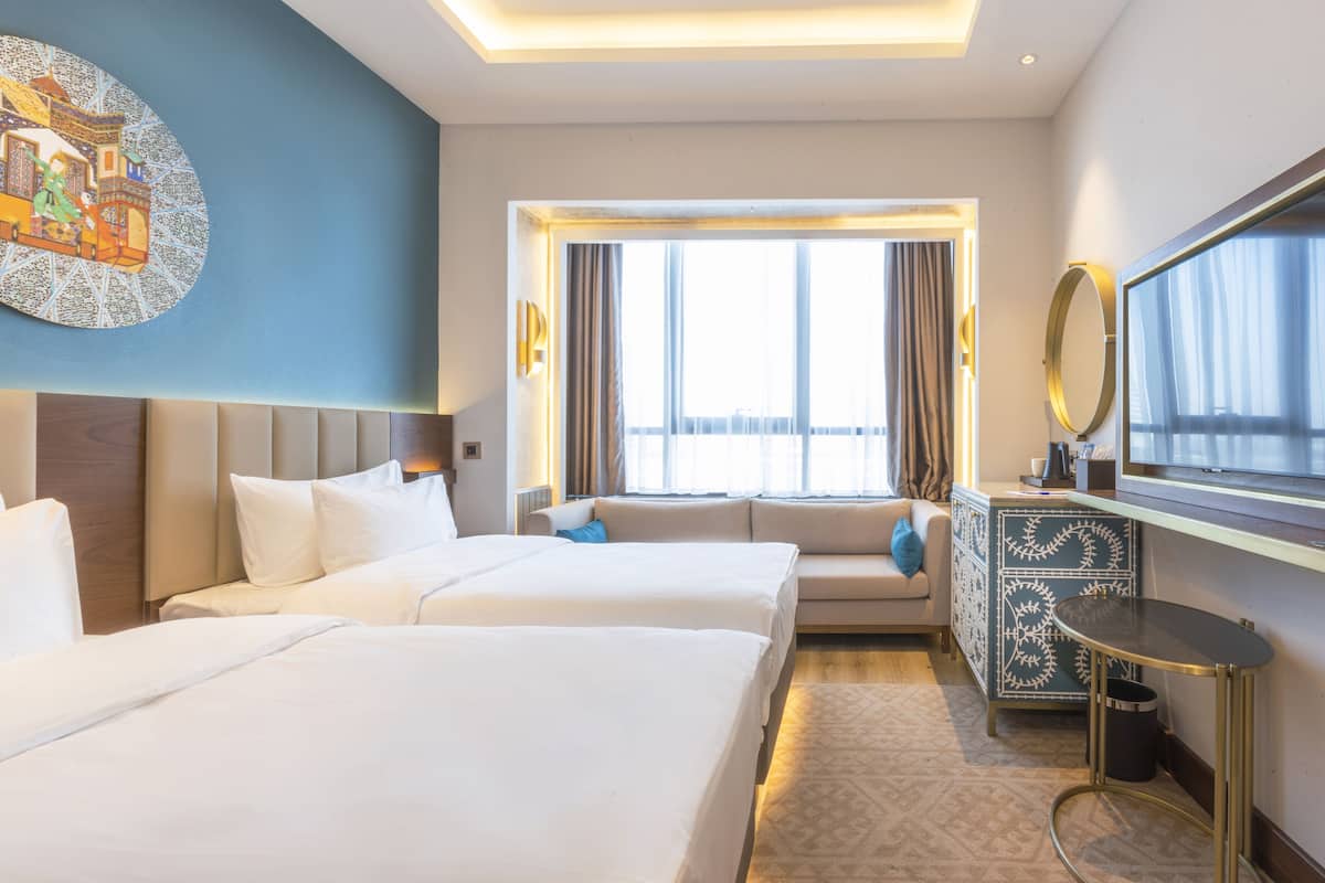 A hotel room with two beds, a sofa, a TV, a decorative wall piece, and a window with curtains.
