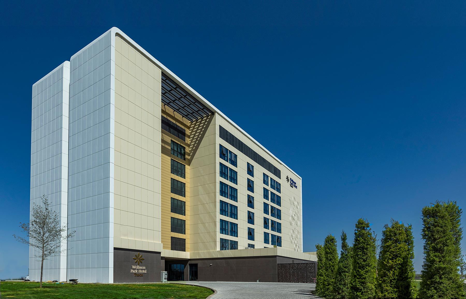 Um hotel moderno com uma entrada de canto imponente, fachada em vidro ampla e área ajardinada com árvores.