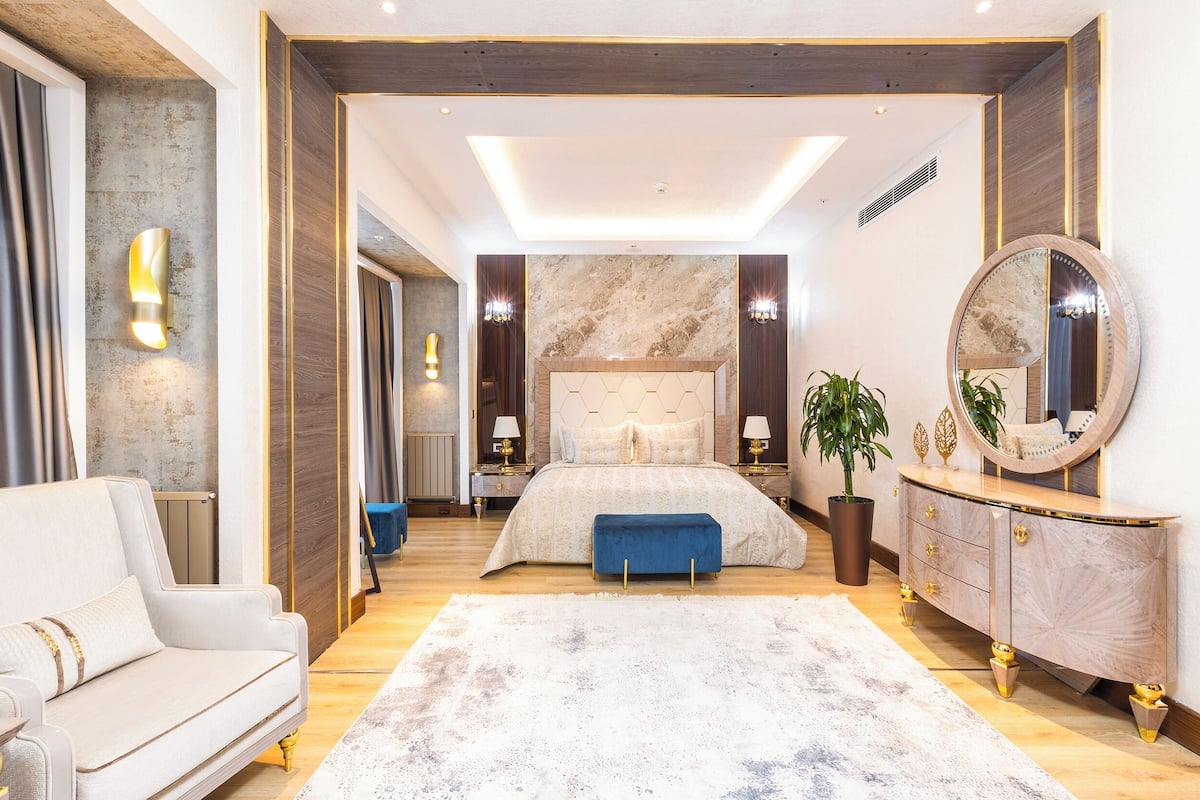 A modern bedroom with a large bed, a sofa, a dresser, and a mirror.