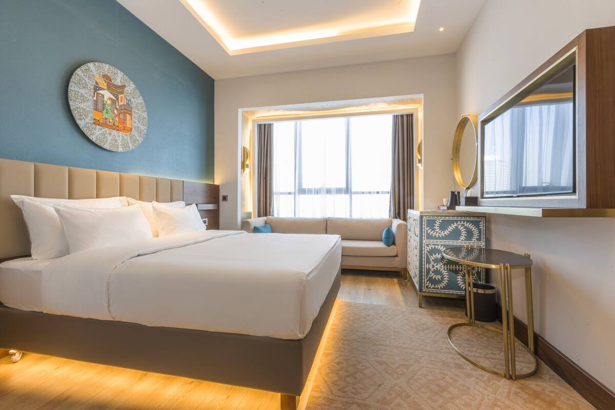 A modern hotel room with a large bed, a sofa, a small table, and a mirror.