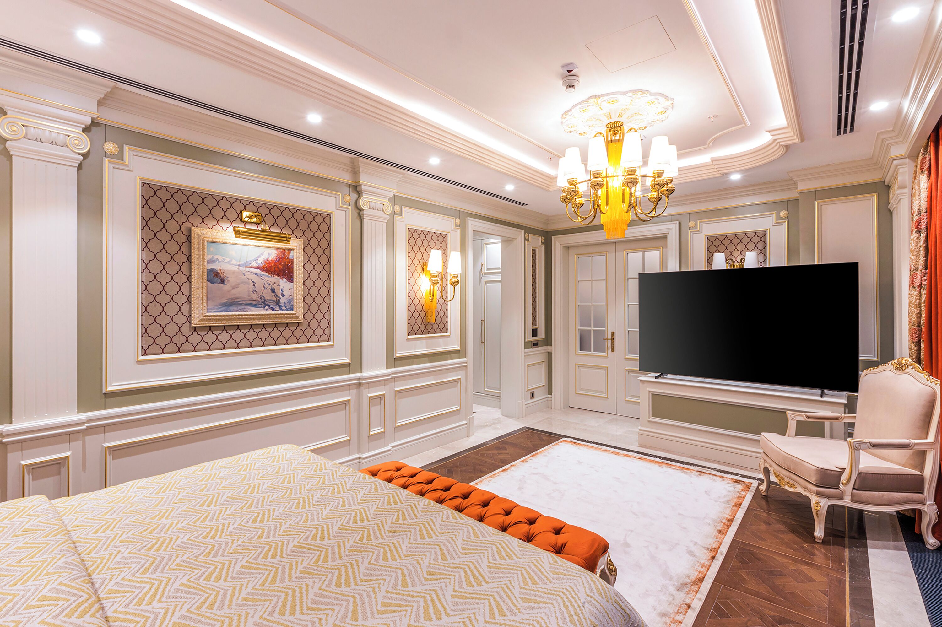 A spacious bedroom with a large bed, a flat-screen TV, and a chandelier.