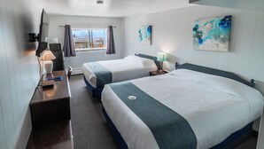 A hotel room with two beds, a desk with a lamp, a TV, and artwork on the walls. - Uptowner Hotel (Creston)