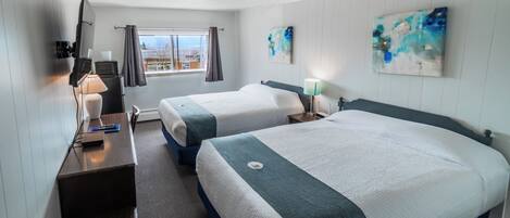 A hotel room with two beds, a desk with a lamp, a TV, and artwork on the walls.