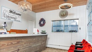 A hotel reception area with a wooden reception desk, a chandelier, a clock, and a window with a view. - Uptowner Hotel (Creston)
