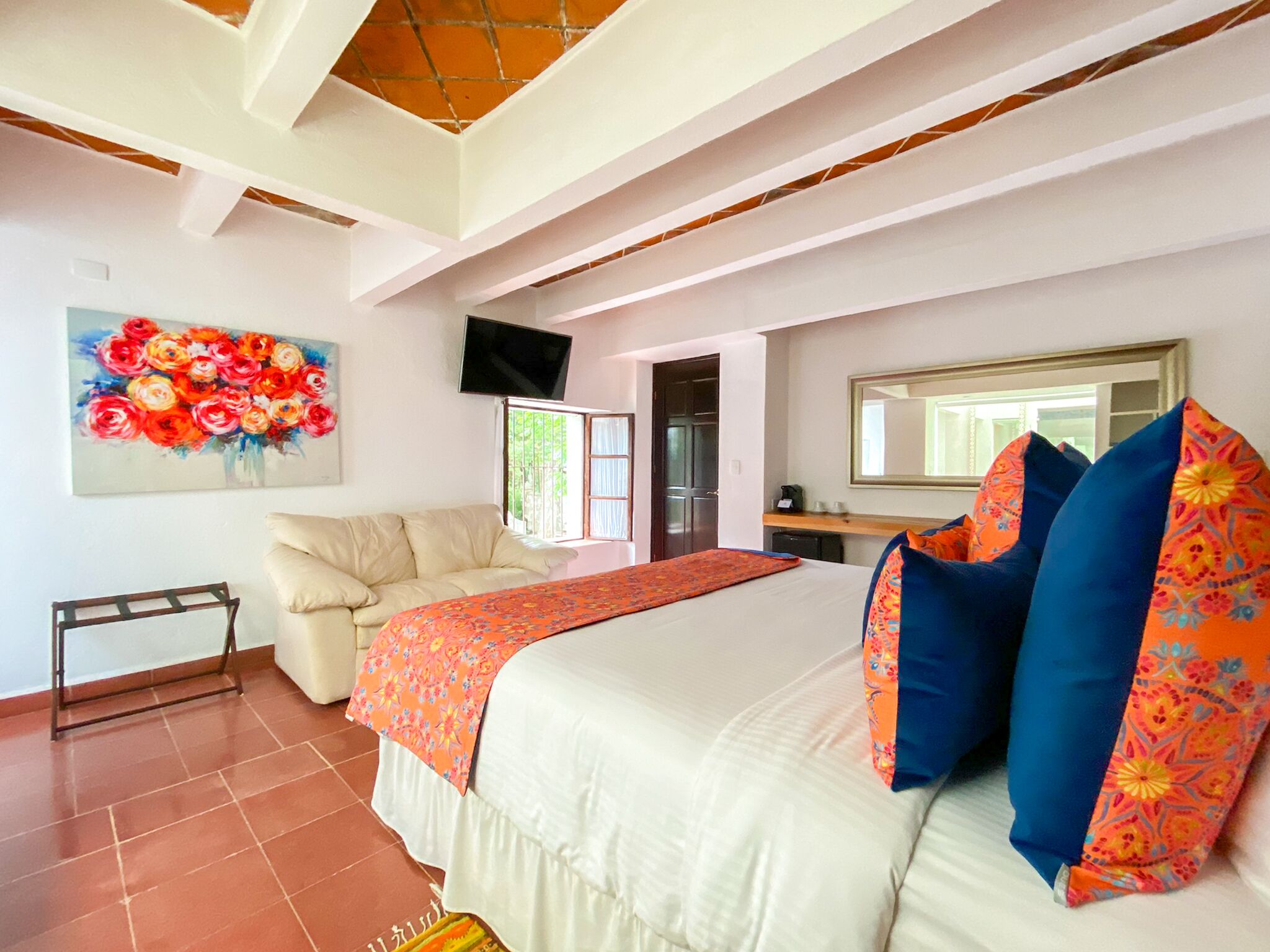 A bedroom with a bed, a sofa, a TV, and a painting.
