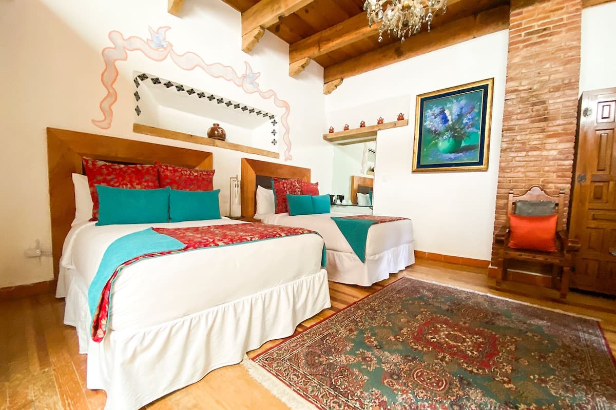 A double room with two beds, a large rug, a wooden ceiling, a mirror, and a painting.