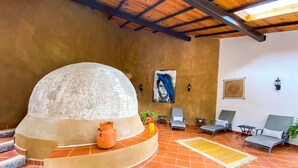 Un espacio interior acogedor con un horno de piedra, asientos cómodos y decoración mural.