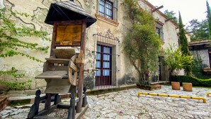 Un edificio rústico con fachada de piedra, escalones de madera que conducen a una puerta y un pozo.