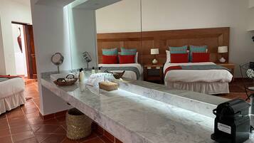 A hotel room with a large mirror, a marble countertop, a bed with patterned pillows, a bedside table with a lamp, and a trash bin.