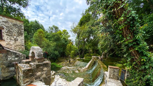 Una estructura de piedra histórica con un canal de agua, rodeada de abundante vegetación.