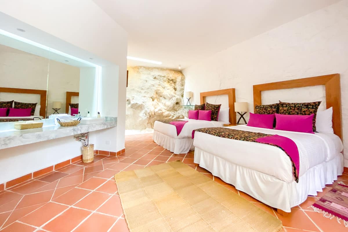 A hotel room with two beds, a large mirror, a stone wall, and a tiled floor.