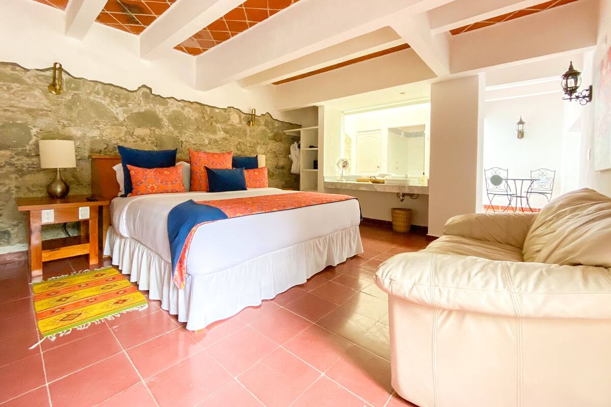 A bedroom with a bed, a nightstand, a lamp, a window, and a view of the dining area.