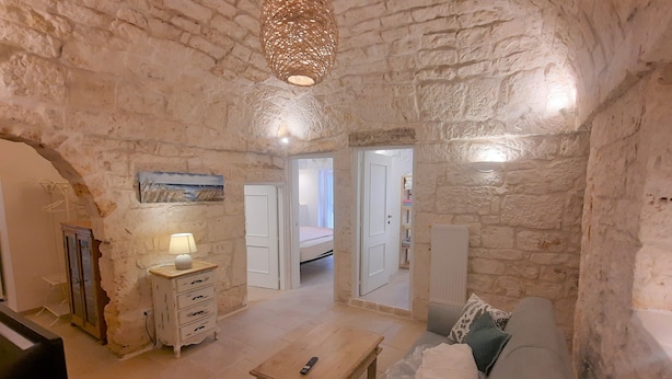 A rustic stone-walled room with a wooden bench, a dresser, and a hanging light fixture.