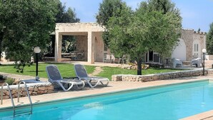 A swimming pool with lounge chairs, a stone building, and a well-maintained garden.