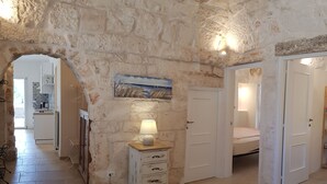 A stone-walled hallway with a white dresser, a lamp, and a painting on the wall.