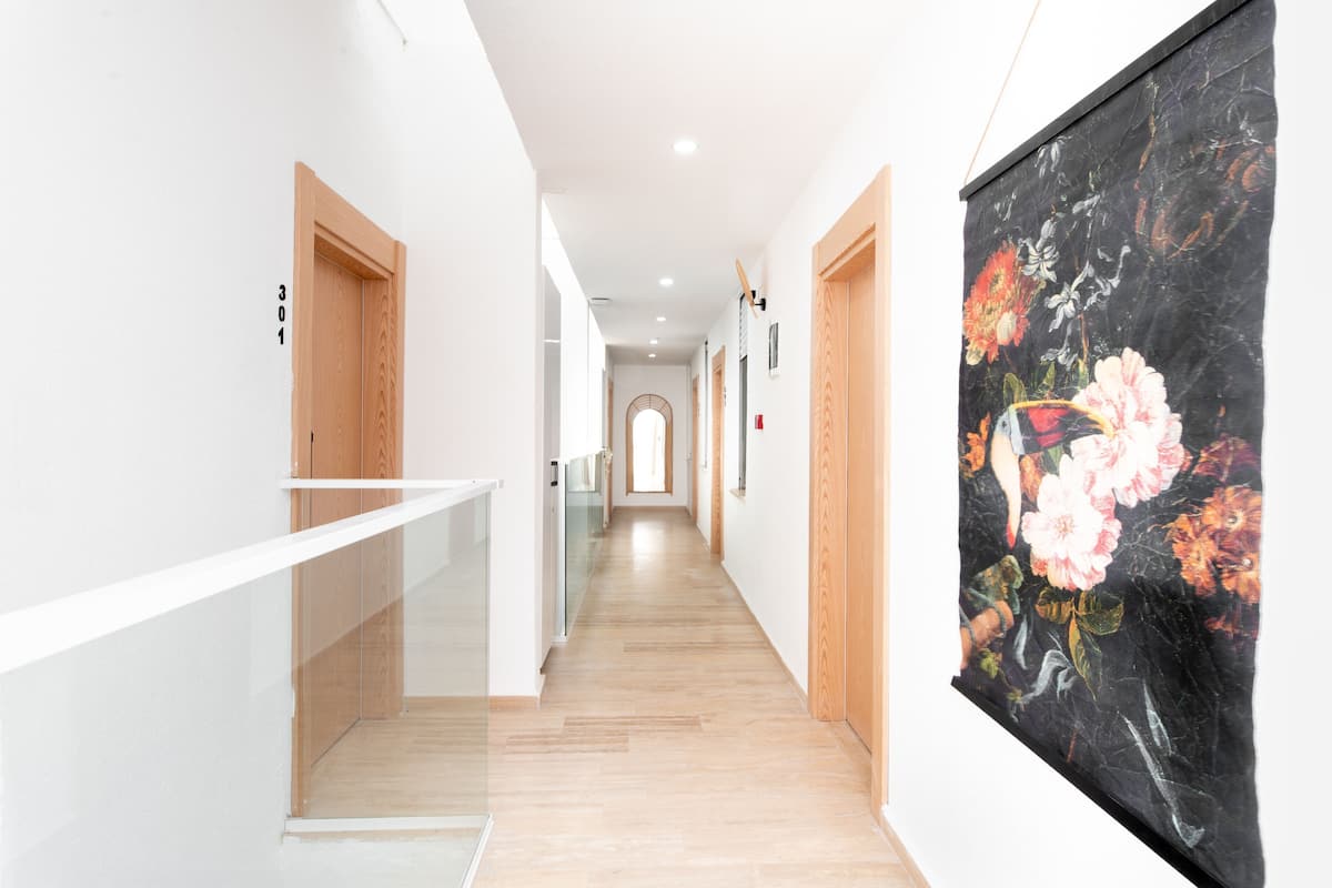 A modern hallway with wooden flooring, white walls, and a large floral artwork on the right.