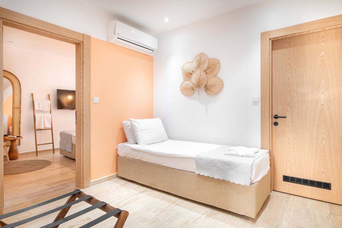 A compact bedroom with a single bed, a wall-mounted air conditioner, and a wooden door.