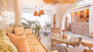 A spacious living area with a sofa, chairs, a glass coffee table, and a dining table. There is a large window with curtains, a plant, and a decorative wall with woven elements. - MARE MARIN BOUTIQUE HOTEL (Bodrum)