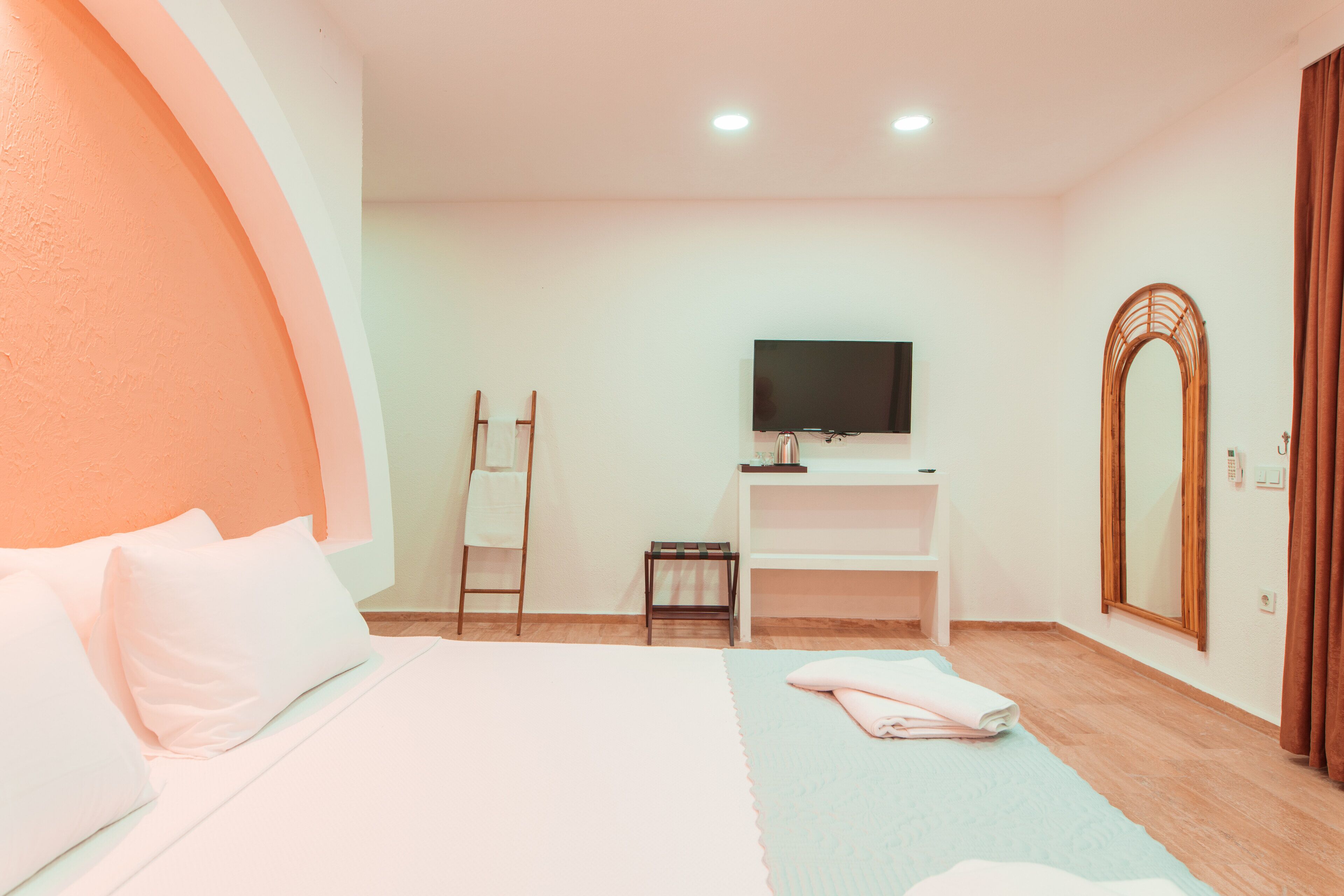A hotel room with a bed, a TV, a mirror, and a small table.