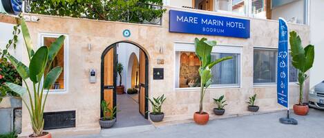 Exterior del Hotel Mare Marin Bodrum, destacando una entrada imponente con un amplio arco, plantas en macetas y una vista despejada del interior a través de la puerta.
