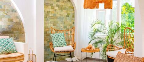A modern interior with wicker furniture, a glass table, and a view of greenery outside.