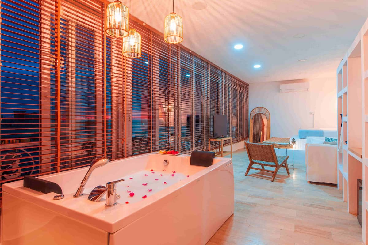 A modern bathroom with a large bathtub, wooden blinds, and pendant lighting.