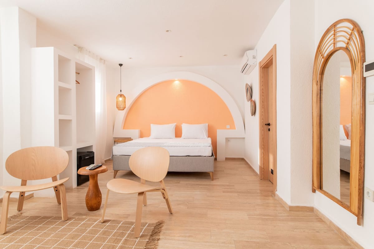 A modern bedroom with a bed, two chairs, a small table, and a mirror.