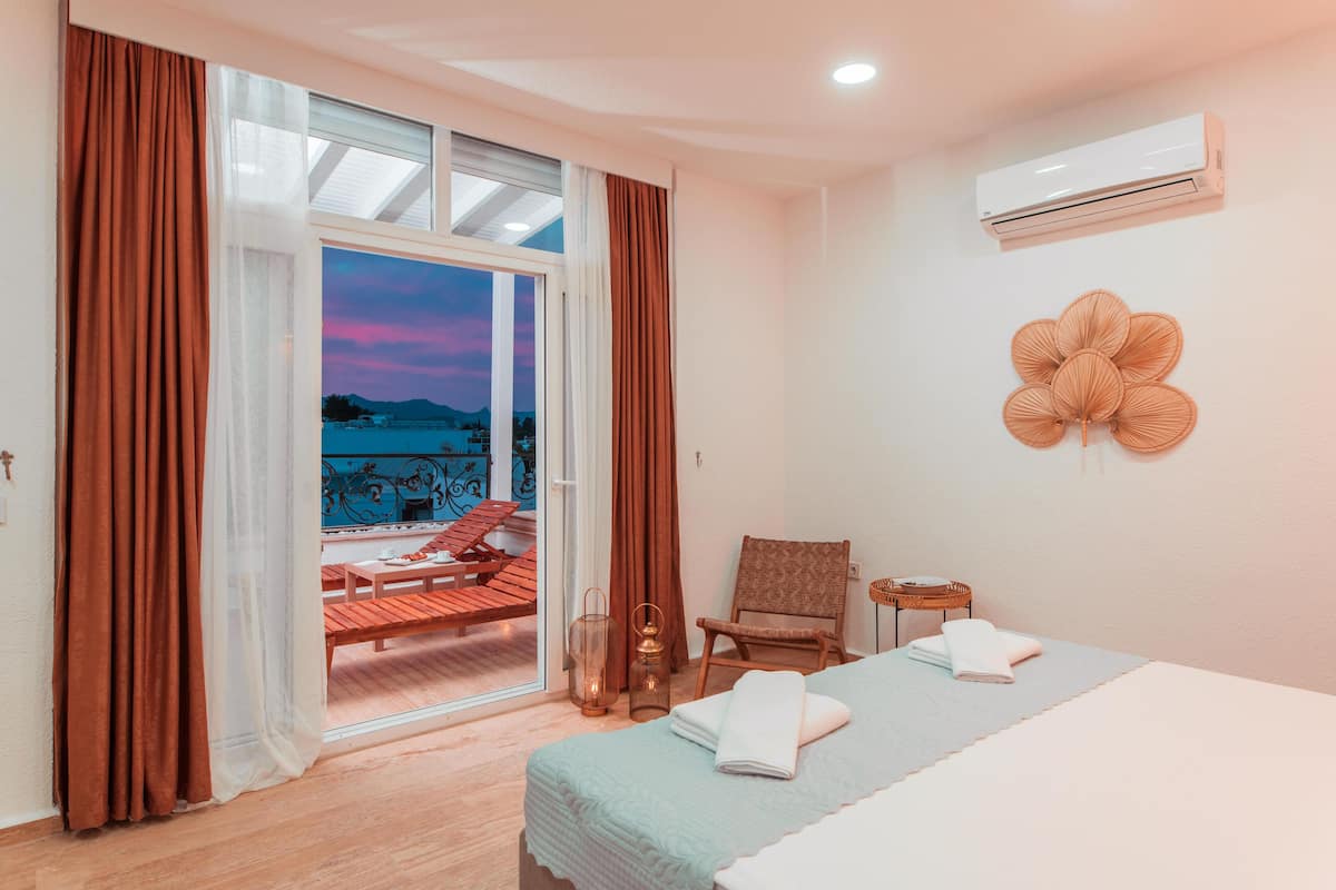 A hotel room with a bed, a chair, a table, and a view of the outside.