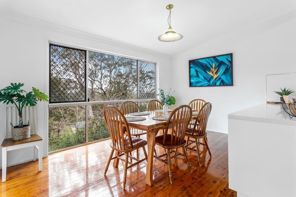 A dining area with a wooden table and chairs, large windows, and a ceiling light.