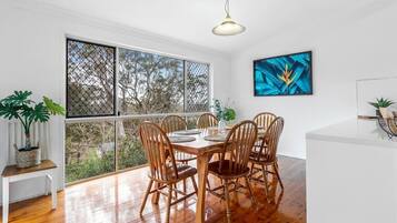 A dining area with a wooden table and chairs, large windows, and a ceiling light.