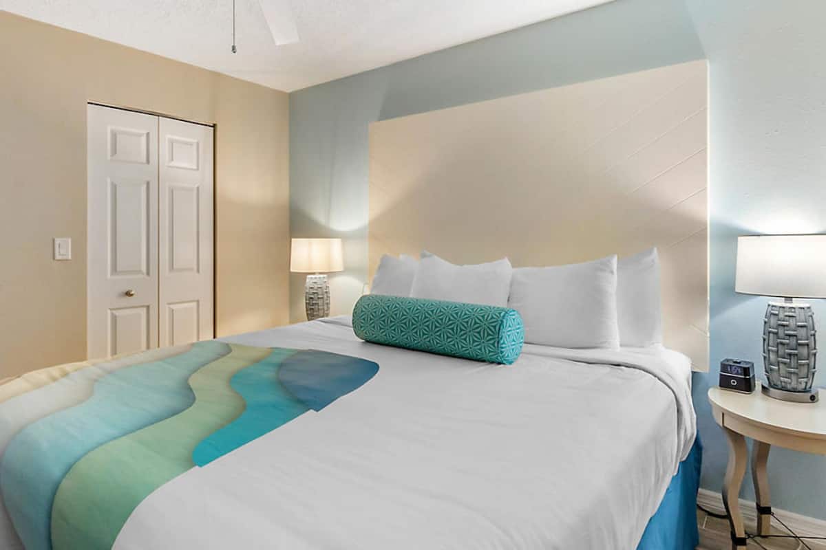 A hotel room with a bed, a nightstand, a lamp, and a door.