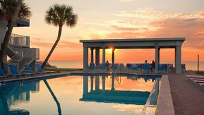 Piscina com cadeiras de descanso e área coberta ao pôr do sol.