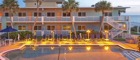 A hotel with a swimming pool, lounge chairs, and palm trees.