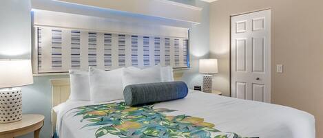 A hotel room with a large bed, a headboard with a lighted panel, a bedside table with a lamp, and a door.