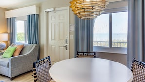 Quarto com mesa redonda, duas cadeiras, sofá, luminária e vista para o exterior.