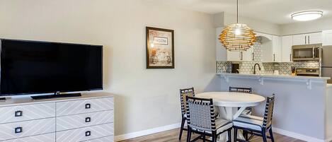 Una cocina moderna con zona de comedor, que incluye un televisor de pantalla plana, una mesa de comedor con sillas y una lámpara colgante.