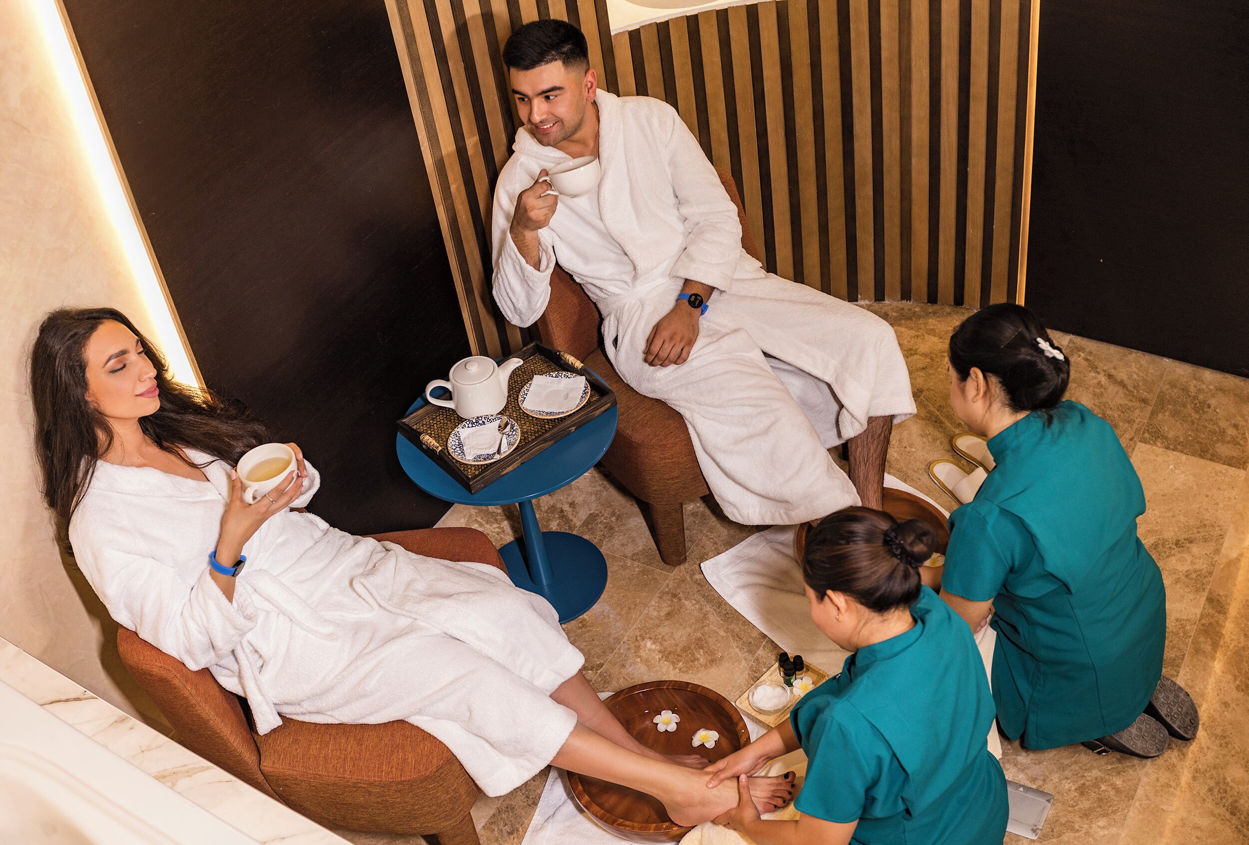 A spa setting with a massage table, a foot massage table, and a small table with a cup and saucer.
