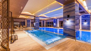 An indoor swimming pool with a tiled floor, surrounded by wooden flooring and walls with a marble-like finish. - Hilton Samarkand Regency (Samarkand)